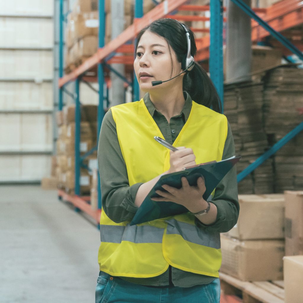 Logistikleiterin mit Headset und Klemmbrett koordiniert Abläufe im Lager