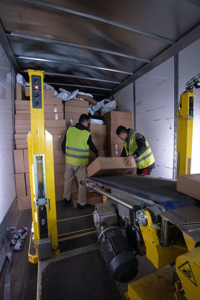 Mitarbeiter entlädt Kartons aus Container mit mobilem Fördersystem von HtW